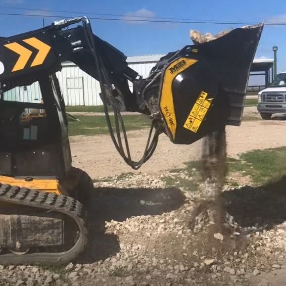 An MB-L160, a skid steer rock crusher processing excavated rocks on a farm.