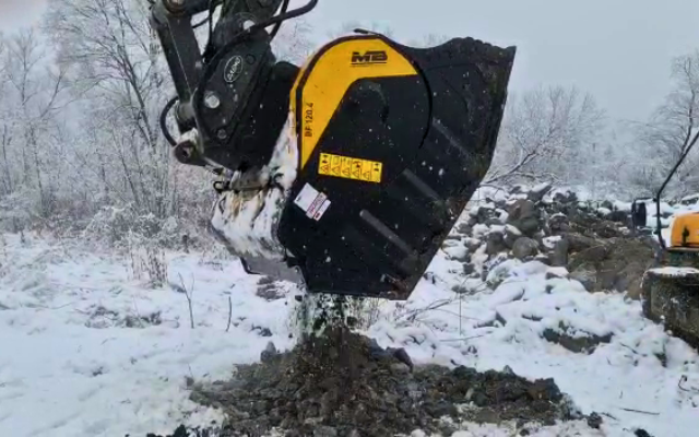 Łyżka Krusząca BF120.4 S4 zamontowana na koparce Hyundai HX300, w akcji na placu budowy, przekształca gruz rozbiórkowy w materiał nadający się do ponownego wykorzystania.