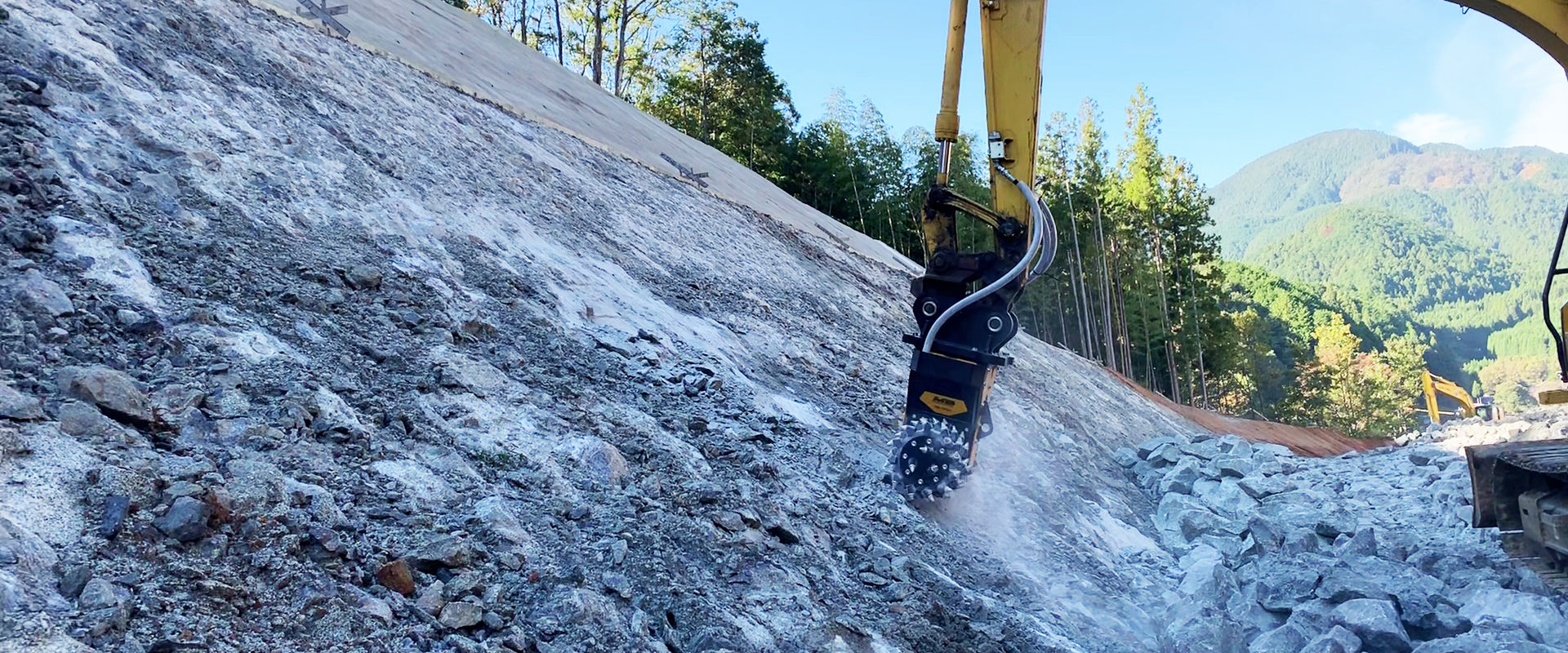 Una fresa idraulica MB-R700 livella le pareti rocciose per l’ampliamento di un tratto di strada in montagna.