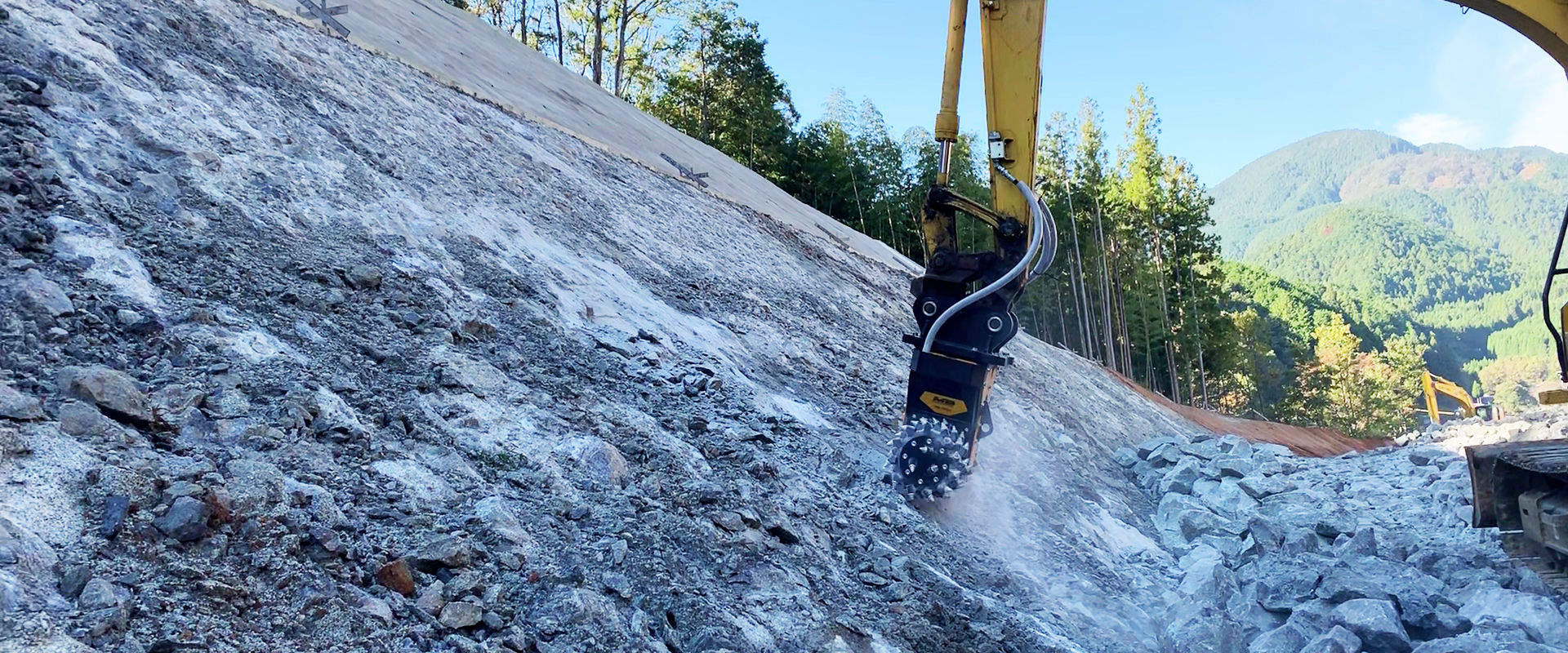 Una fresa idraulica MB-R700 livella le pareti rocciose per l’ampliamento di un tratto di strada in montagna. 